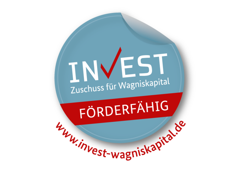 Round blue sticker with a red checkmark in the word "INVEST," text saying "Zuschuss für Wagniskapital," a red banner with "FÖRDERFÄHIG," and the website www.invest-wagniskapital.de curved around the bottom.